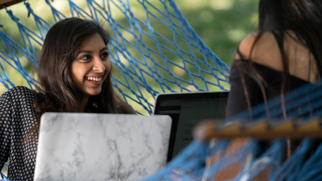 Student smiling in hamock using laptop.