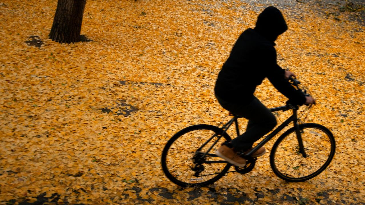 student riding a bike through the fall leaves