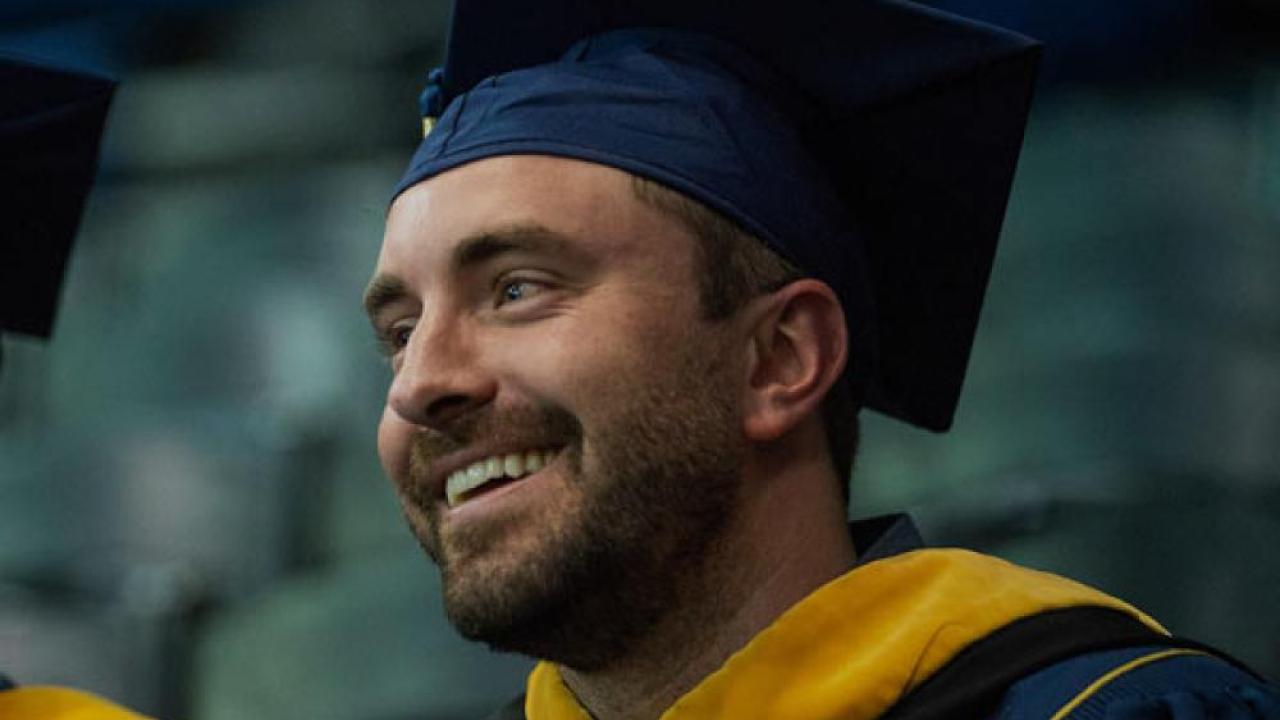A UC Davis student smiles in graduation regalia